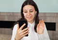 Young woman is making a video call on her smartphone. In room. There is a earphones in the woman`s ears Royalty Free Stock Photo