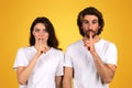 A young woman and a man with dark hair and white t-shirts gesture for silence Royalty Free Stock Photo