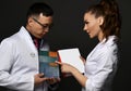 Young woman and man doctors in white medical uniform gown discuss professional books with blank cover they hold in hands