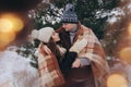 A young woman and a man hug under a cozy checkered blanket