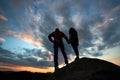 Young woman and man standing on the rock and watching for running clouds. With beautiful sunset on background.