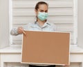 A young woman in a mask shows a finger on a blank cork board, standing on a white background. Copy space on whiteboard for image o Royalty Free Stock Photo