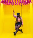 Young woman with mask on swing with yellow background