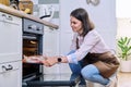 Young woman with meat on baking tray opening oven, kitchen at home Royalty Free Stock Photo