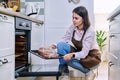Young woman with meat on baking tray opening oven, kitchen at home Royalty Free Stock Photo