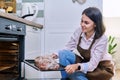 Young woman with meat on baking tray opening oven, kitchen at home Royalty Free Stock Photo