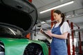 Young woman mechanic writing on clipboard at repair garage Royalty Free Stock Photo