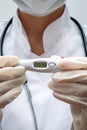 A young woman medic holds an electronic thermometer in her hands which shows the word COVID on the display. The concept of
