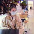 Young woman in a medical face mask at a table in a christmas restaurant. Living with the coronavirus pandemic