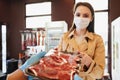 Young woman in medical mask buying raw meat in grocery store Royalty Free Stock Photo