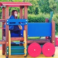 Young woman in a medical mask on a children playground in a toy train Royalty Free Stock Photo