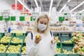 Young woman in a medical mask chooses apples in a supermarket. Healthy eating. Coronavirus pandemic