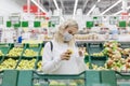 Young woman in a medical mask chooses apples in a supermarket. Healthy eating. Coronavirus pandemic