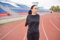 Young woman in medical mask doing warm-up at stadium. Adult female in black casual clothes doing sports in fresh air and