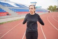 Young woman in medical mask doing warm-up at stadium. Adult female in black casual clothes doing sports in fresh air and