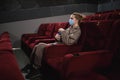 young woman in medical mask eating popcorn sitting in the cinema Royalty Free Stock Photo