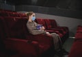 Young woman in medical mask eating popcorn sitting in the cinema Royalty Free Stock Photo