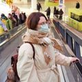 Young woman in medical mask on escalator in shopping mall store