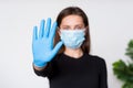 Young woman in medical mask and gloves shows stop sign by her hand