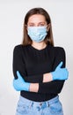 Young woman in medical mask and gloves standing with arms crossed on her chest, white background