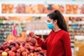 A young woman in a medical mask on her face looking at apples in a supermarket. The concept of shopping and the new