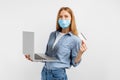 Young woman in a medical mask on her face, shows a plastic credit card and uses a laptop, on a white background