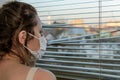 Young woman in medical mask looks out the window through the blinds Royalty Free Stock Photo