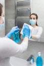 Young woman with medical mask polishing mirror with rag and using disinfectant spray. Housekeeping and cleaning service Royalty Free Stock Photo