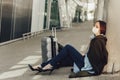 Young woman in medical mask sits near luggage in airport. Tortured by the flight, the woman dozes off