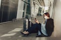 Young woman in medical mask sits near luggage in airport. Woman waiting for flight, using a cell phone and Royalty Free Stock Photo