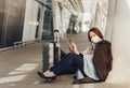 Young woman in medical mask sits near luggage in airport. Woman waiting for flight, using a cell phone Royalty Free Stock Photo