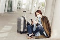 Young woman in medical mask sits near luggage in airport. Woman waiting for her flight, using a mobile phone Royalty Free Stock Photo