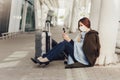 Young woman in medical mask sits near luggage in airport. Woman waiting for her flight, using a mobile phone Royalty Free Stock Photo