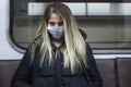 A young woman in a medical mask sits in a subway car. Beautiful blonde in a black jacket. Protection during the coronavirus
