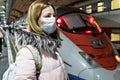 A young woman in a medical mask stands on the platform of the station waiting for the departure of a high-speed train. The Royalty Free Stock Photo