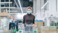 A woman in a medical mask stands in a supermarket with a timelapse grocery cart. Protection from coronavirus, buying Royalty Free Stock Photo