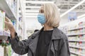 Young woman in a medical mask in a supermarket chooses cleaning products. Beautiful blonde. Coronavirus pandemic Royalty Free Stock Photo