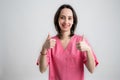 Young woman medical professional nurse or doctor dressed with pink hospital clothes showing thumbs up with both hands Royalty Free Stock Photo