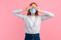 Young woman in a medical protective mask covers her eyes with her hands on an isolated pink background. Quarantine, coronavirus Royalty Free Stock Photo