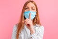 Young woman in a medical protective mask on her face, holds her front finger over her lips, makes a gesture of silence, speaks Royalty Free Stock Photo