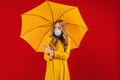 Young woman in a medical protective mask on her face, with an umbrella in her hands on a red background Royalty Free Stock Photo