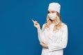 Young woman in medical uniform and face mask posing at blue background, . Nurse or doctor in a white medical Royalty Free Stock Photo