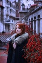 A young woman in a medieval dress walks through a field in a warm winter cloak with fur. medieval palace in the background