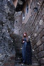 A young woman in a medieval dress walks through a field in a warm winter cloak with fur. medieval palace in the background