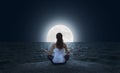 Young woman meditating on the beach at full moon