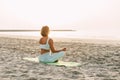 Young woman meditating in pose of lotus on beach near the sea at sunset in summer, rear view Royalty Free Stock Photo