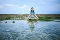 Young woman, meditating, practicing yoga and pranayama at the beach. Sunset yoga practice. Hands in gyan mudra. Water reflection. Royalty Free Stock Photo
