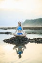 Young woman, meditating, practicing yoga and pranayama at the beach. Sunset yoga practice. Hands in gyan mudra. Water reflection. Royalty Free Stock Photo