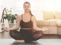 Young woman in meditative position practicing yoga at home - beautiful girl meditates sukhasana posture relaxation - healthy