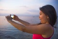 Young woman with mobile phone camera taking picture of beautiful beach sunset landscape and mount Agung volcano of Bali in Asia ho Royalty Free Stock Photo